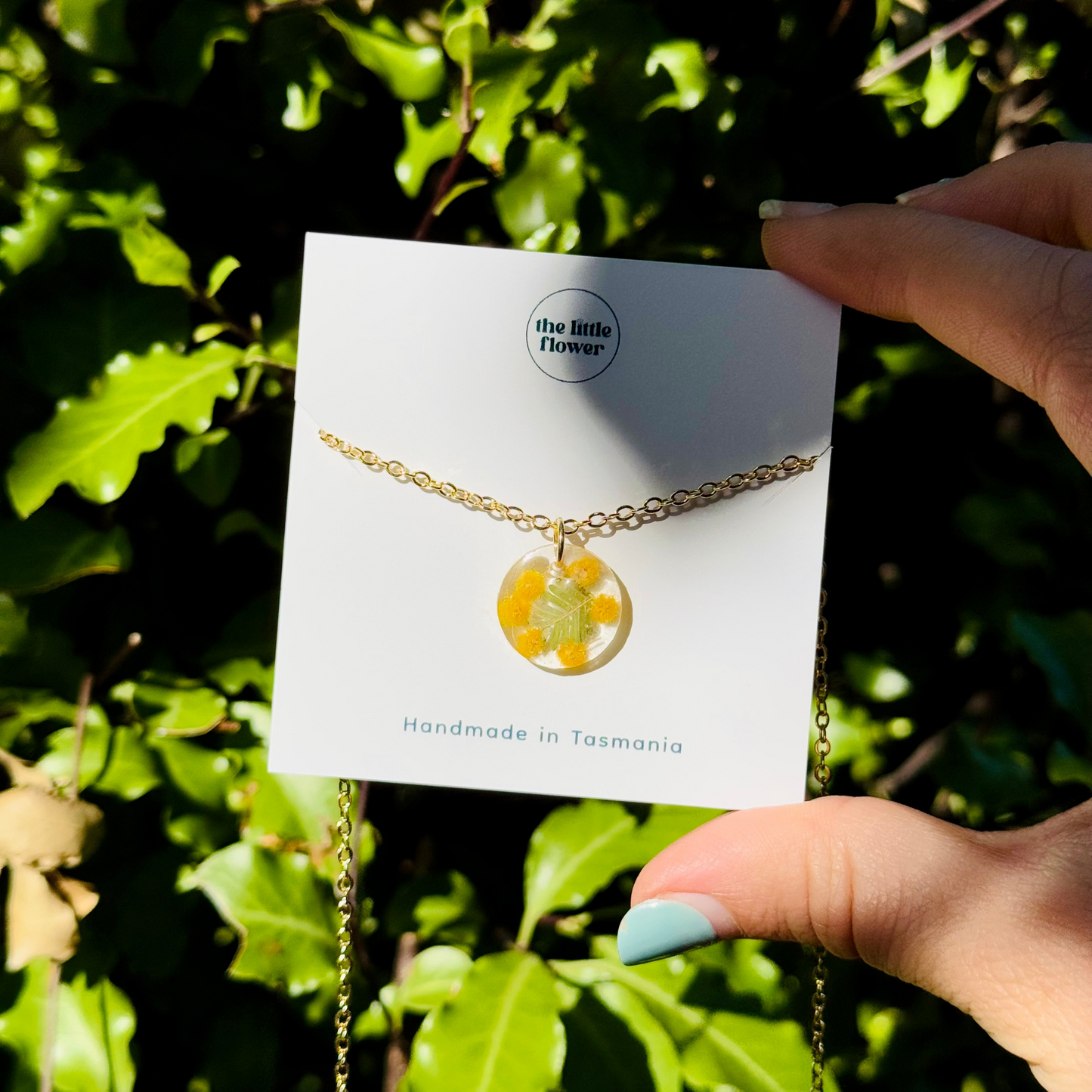 Small round resin pendant with real native wattle flowers, held in hand for size reference