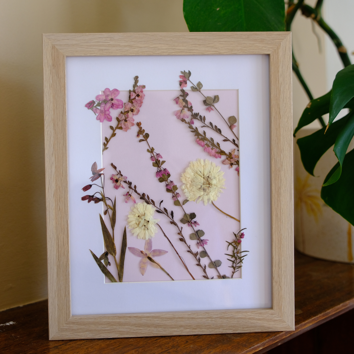 Framed artwork with pressed flowers on a wooden surface